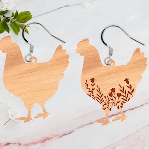 Könnte beinhalten: Ein Paar Hühnerohrringe aus Holz. Ein Ohrring ist aus einfachem Holz, während der andere ein braunes Blumenmuster hat.