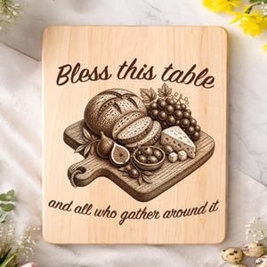May include: Wooden cutting board with a handle, engraved with the words "Bless this table and all who gather around it." The board features an engraved illustration of bread, grapes, cheese, olives, and figs.
