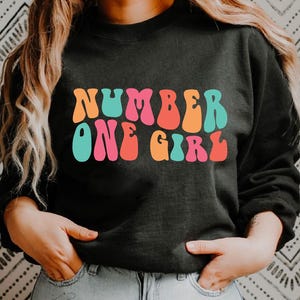 Número uno chica SVG y PNG para sublimación: diseño lindo y atrevido para camisetas, tazas, bolsos y más. Divertidas letras onduladas apiladas.