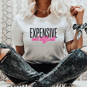 May include: White t-shirt with black text that reads "EXPENSIVE and difficult" in pink lettering.