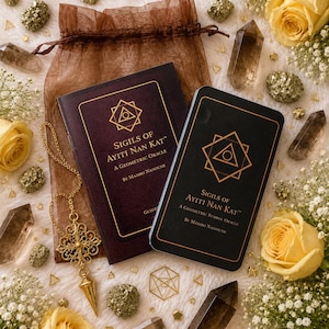 May include: A Sigils of Ayiti Nan Kat oracle deck with a guidebook, a gold-toned metal pendulum, and a brown organza drawstring bag. The set is surrounded by yellow roses, baby's breath, smoky quartz crystals, and small gold-colored geometric charms.