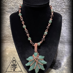 May include: A handcrafted necklace featuring a green leaf pendant wrapped in copper wire. The necklace includes green and black beaded accents, and is displayed on a black bust. The logo "CosmicJewelz777" is visible.