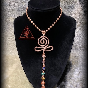 May include: Copper wire pendant necklace with a spiral design and a beaded chain. The pendant features a series of colorful gemstones. The necklace is displayed on a black mannequin. The text "CosmicJewelz777" is visible.