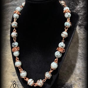 May include: A beaded necklace with light gray and black speckled beads, strung together with copper wire. The necklace is displayed on a black jewelry bust. The bottom left corner has the text "CosmicJewelz777".