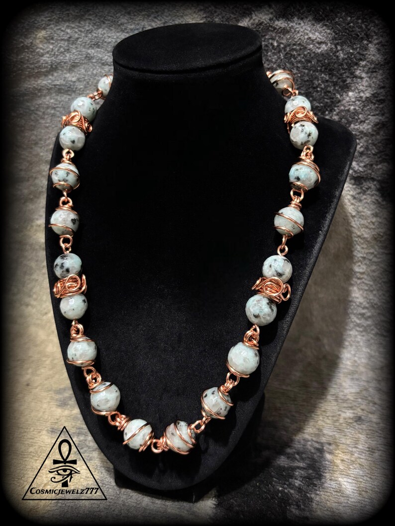 May include: A beaded necklace with light gray and black speckled beads, strung together with copper wire. The necklace is displayed on a black jewelry bust. The bottom left corner has the text "CosmicJewelz777".