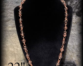 May include: A 22-inch necklace featuring clear, spherical beads individually encased in a copper wire cage. The beads are connected by copper jump rings, creating a continuous chain design that hangs in a circular shape.