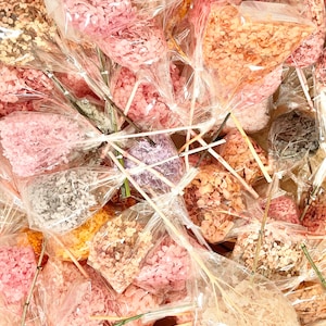 May include: A variety of dried hydrangea flower heads in different colors, including pink, white, and purple, are packaged in clear plastic bags. The flower heads are arranged in bouquets and tied with twine.