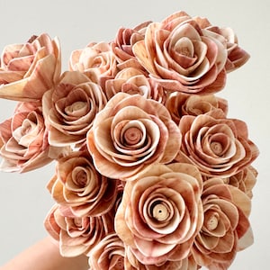 May include: A bouquet of 15 faux wooden roses in shades of brown and pink. The roses are arranged in a hand, with the stems facing down.