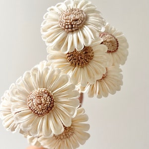 May include: A bouquet of six cream-colored sola wood flowers with brown centers. The flowers are arranged in a hand-held bouquet.
