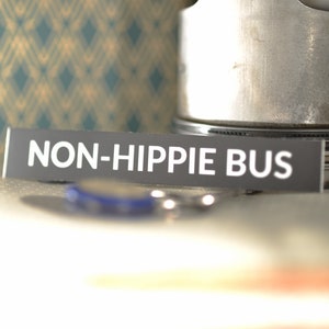 May include: A black and white sticker with the text "NON-HIPPIE BUS" on a gray background.