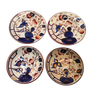 May include: Four decorative ceramic plates with a white background, featuring a blue and orange floral design. The plates have a dark brown rim and are arranged in a square formation. Each plate has a unique pattern.