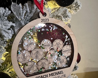 Könnte beinhalten: Ein hölzerner Weihnachtsbaumschmuck mit einem durchsichtigen Plastikfenster, das mit roten und grünen Glitzer gefüllt ist. Der Schmuck trägt das Jahr 2023, die Namen eines Fußballteams und den Text "COACH MICHAEL ALLIANCE U10 ELITE", der darauf graviert ist.
