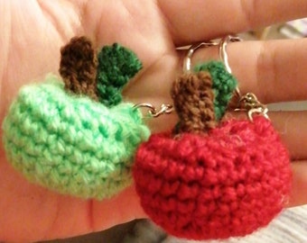 May include: A green and red crocheted apple keychain. The keychain is made of yarn and has a silver metal ring.
