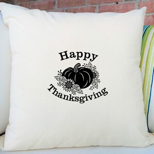 Peut inclure: Un coussin blanc avec du texte noir qui dit "Joyeux Thanksgiving" et une silhouette noire d'une citrouille avec des fleurs.