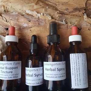 May include: Three glass bottles with dropper tops containing herbal tinctures and sprays. The bottles are labelled "Sonnengarten Farm" and feature the text "Herbal Support Tincture", "Herbal Syrup", and "Herbal Spray".
