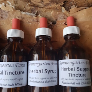 May include: Three glass bottles with dropper tops filled with brown liquid. The bottles are labeled "Sonnengarten Farm Herbal Syrup", "Sonnengarten Farm Herbal Support Tincture", and "Engarten Farm Herbal Tincture". Each bottle has a label with the text "Only pure herbs organic or wild crafted. Handarbeit mit Liebe 100ml".