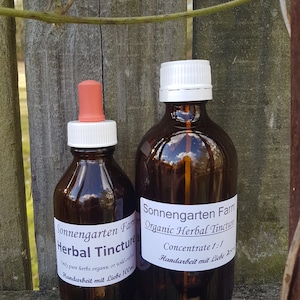 May include: Two amber glass bottles with white labels and black text. The smaller bottle is 100 ml and the larger bottle is 200 ml. Both bottles contain organic herbal tinctures. The labels read "Sonnengarten Farm Herbal Tincture" and "Sonnengarten Farm Organic Herbal Tincture".