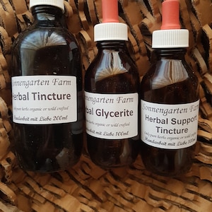 May include: Three amber glass bottles with dropper tops containing herbal tinctures. The bottles are labelled "Sonnengarten Farm" and have the text "Herbal Tincture", "Herbal Glycerite", and "Herbal Support Tincture". Each bottle has a label with the text "Only pure herbs organic or wild crafted" and "Handarbeit mit Liebe" followed by the volume in millilitres.