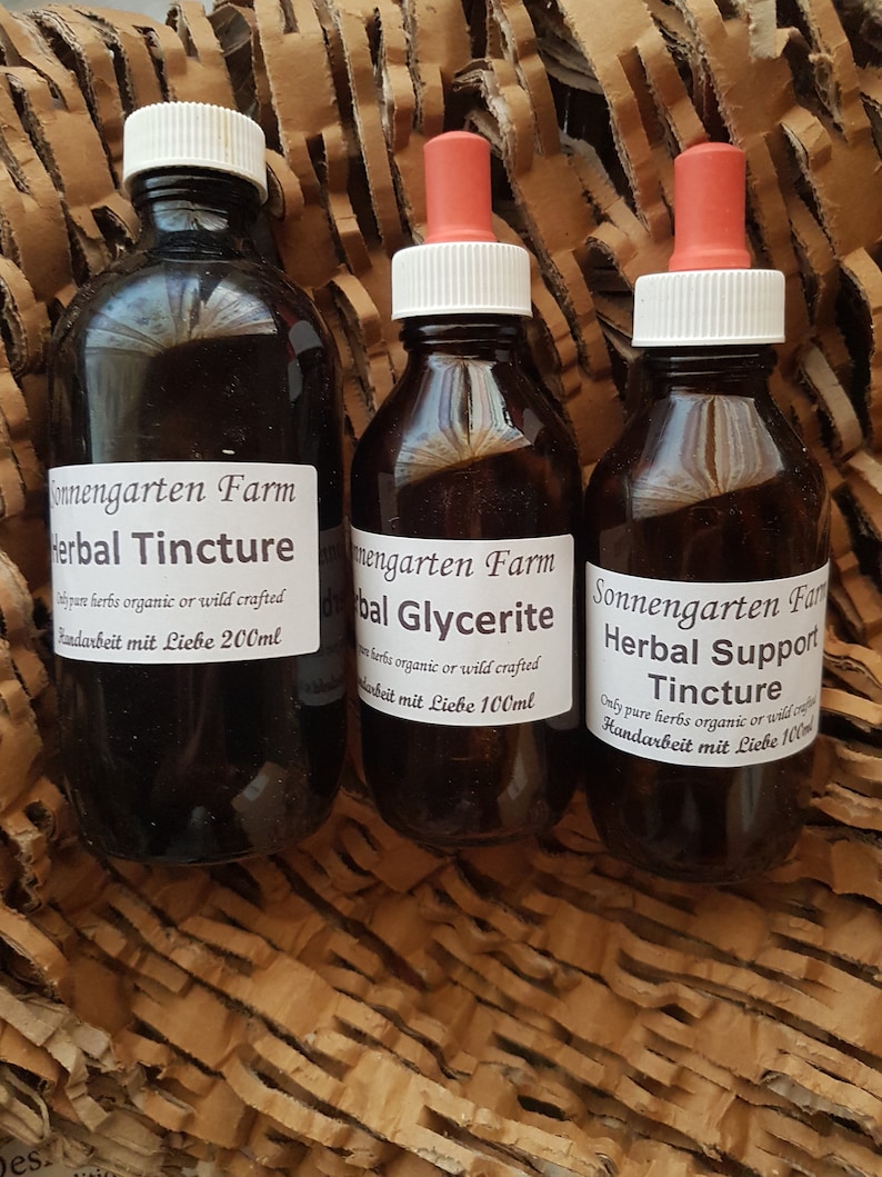May include: Three amber glass bottles with dropper tops containing herbal tinctures. The bottles are labelled "Sonnengarten Farm" and have the text "Herbal Tincture", "Herbal Glycerite", and "Herbal Support Tincture". Each bottle has a label with the text "Only pure herbs organic or wild crafted" and "Handarbeit mit Liebe" followed by the volume in millilitres.