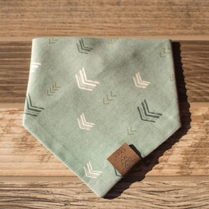 May include: A light green bandana with a white and green arrow pattern. The bandana has a brown leather tag with a flower design.