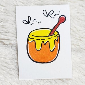 May include: A hand-drawn illustration of a honey pot with a red spoon. The pot is orange with yellow honey dripping down the sides. Two small black bees are flying above the pot. The image is on a white background.