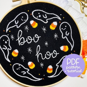 Pode incluir: Arte de bordado em aro com fundo preto e fantasmas brancos, milho doce e o texto "boo hoo". Um círculo roxo com o texto "Padrão PDF + tutorial" está no canto inferior direito.
