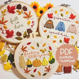 Könnte beinhalten: Drei Stickrahmen-Kunstwerke mit Herbstmotiven. Der erste Rahmen sagt "Herbst ist da" mit Herbstblättern und Eicheln. Der zweite Rahmen sagt "Pulloverwetter" mit drei Pullovern und Herbstblättern. Der dritte Rahmen sagt "Fühle mich Kürbis-geil" mit Kürbissen und Herbstblättern.