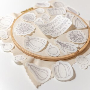 May include: A set of embroidery patterns featuring fall-themed designs, including pumpkins, sunflowers, apples, corn, and gourds. The patterns are printed on white fabric and are ready to be stitched.