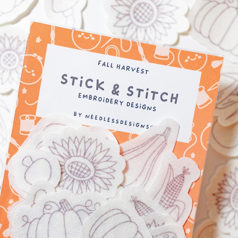 May include: A set of white felt embroidery designs with an orange background. The designs include a sunflower, pumpkin, corn, and squash. The text on the package reads "Fall Harvest Stick & Stitch Embroidery Designs by Needless Designs".