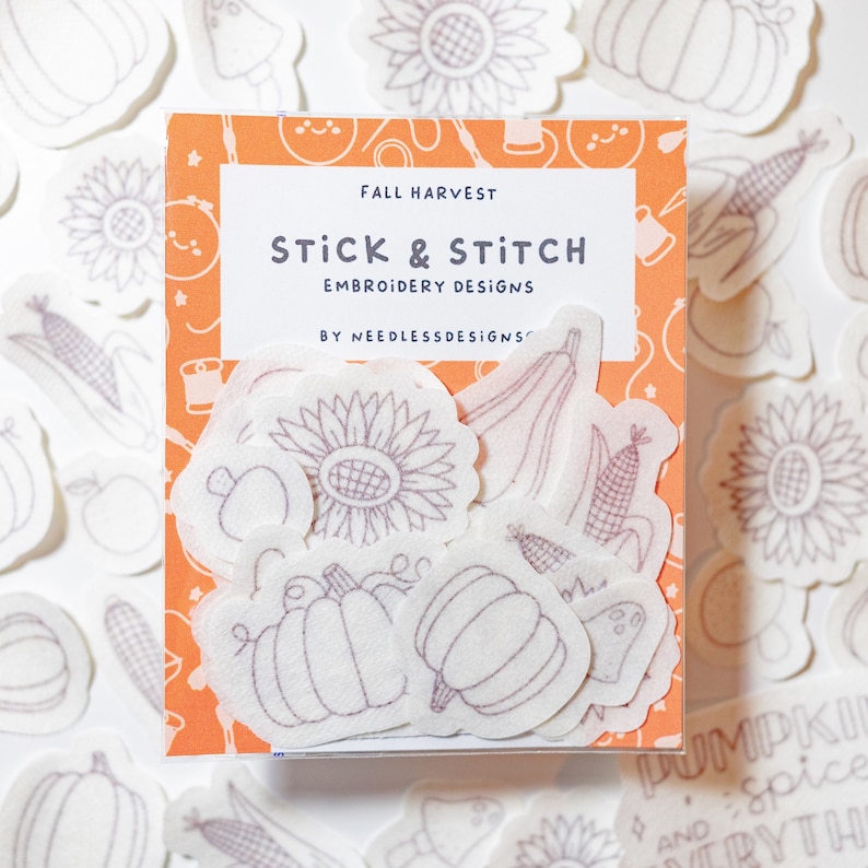 May include: A set of 12 white felt embroidery patterns with fall harvest designs. The patterns include pumpkins, sunflowers, corn, and gourds. The patterns are packaged in a clear plastic box with a colorful label that says "Fall Harvest Stick & Stitch Embroidery Designs by Needless Designs".