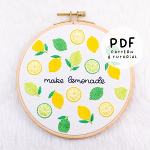 Könnte beinhalten: Stickerei-Hoop-Kunst mit weißem Hintergrund und gelben Zitronen und grünen Limettenscheiben. Der Text "make lemonade" ist in schwarzem Faden gestickt.