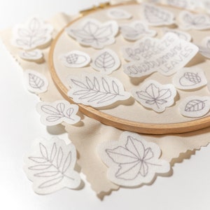 Pode incluir: Uma cole&ccedil;&atilde;o de folhas de outono bordadas e uma placa que diz "Fall breeze and autumn leaves" em um fundo de tecido bege.