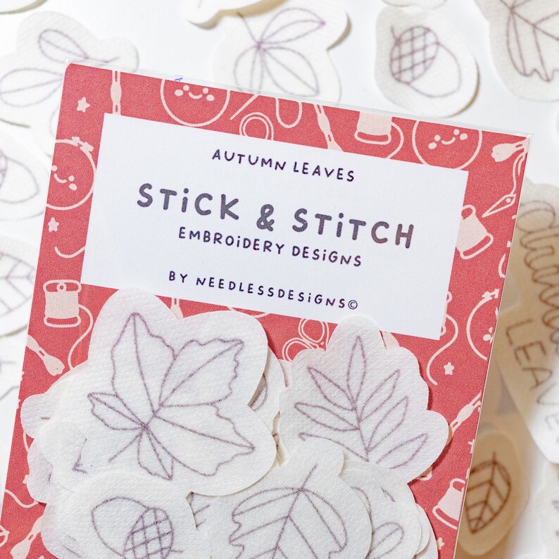 Pode incluir: Um pacote de folhas de outono de feltro branco com desenhos de bordado para um projeto de artesanato de colagem e costura. O pacote &eacute; etiquetado como "Autumn Leaves Stick & Stitch Embroidery Designs by NeedlessDesigns".