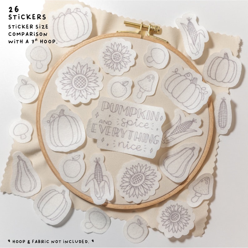 May include: A set of 26 white iron-on stickers featuring various fall-themed designs, including pumpkins, sunflowers, corn, apples, mushrooms, and a text sticker that reads "Pumpkin and spice. Everything nice." The stickers are displayed on a 7-inch embroidery hoop.