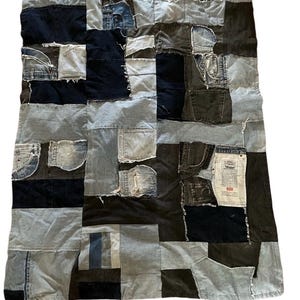 Peut inclure: Une couverture en patchwork rectangulaire composée de divers morceaux de tissu en jean dans des tons bleu, noir et gris. Le motif présente plusieurs panneaux rectangulaires, incluant des poches visibles, des bords effilochés et une étiquette blanche Levi's.