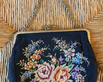 Könnte beinhalten: Eine vintage schwarze Abendtasche mit einer goldenen Kettenkette und einem floralen Stickmuster. Die Stickerei zeigt einen Strauß aus rosa, gelben und orangefarbenen Rosen mit grünen Blättern und lila, blauen und weißen Blumen.