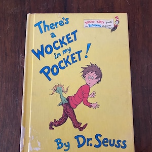 May include: A yellow book cover with the title "There's a WOCKET in my POCKET!" in large, colorful letters. The book is illustrated with a cartoon boy running away from a green creature with a long tail sticking out of his back pocket. The book is by Dr. Seuss and is part of the "Bright and Early Books for Beginning Beginners" series.