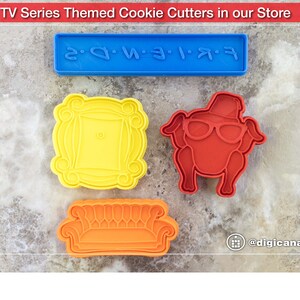 Puede incluir: Cuatro cortadores de galletas en forma de sof&aacute;, marco de fotos, pavo y un letrero que dice "FRIENDS" en pl&aacute;stico azul. Los cortadores de galletas est&aacute;n sobre una superficie gris texturizada.