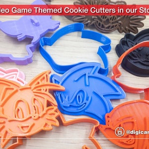 Puede incluir: Un conjunto de cortadores de galletas de pl&aacute;stico de colores con forma de personajes del videojuego Sonic the Hedgehog. Los cortadores incluyen a Sonic, Tails, Knuckles y Amy Rose. Los cortadores est&aacute;n dispuestos sobre una superficie de madera. El texto "@digicanal3d" es visible en la esquina inferior derecha de la imagen.