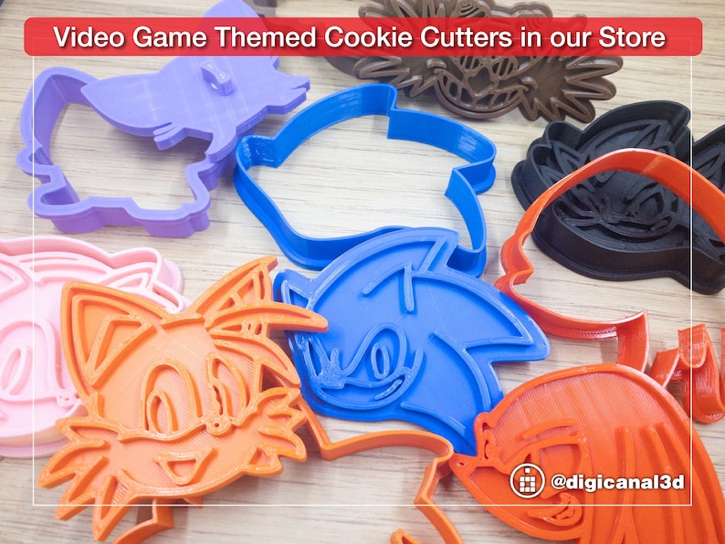Puede incluir: Un conjunto de cortadores de galletas de pl&aacute;stico de colores con forma de personajes del videojuego Sonic the Hedgehog. Los cortadores incluyen a Sonic, Tails, Knuckles y Amy Rose. Los cortadores est&aacute;n dispuestos sobre una superficie de madera. El texto "@digicanal3d" es visible en la esquina inferior derecha de la imagen.