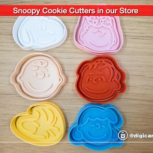 Puede incluir: Conjunto de seis cortadores de galletas de pl&aacute;stico de colores con forma de diferentes personajes de la tira c&oacute;mica Peanuts. Los cortadores est&aacute;n dispuestos sobre una superficie de madera. Los personajes incluyen Snoopy, Woodstock, Charlie Brown, Lucy, Linus y Sally.