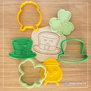 Könnte beinhalten: Ein Set aus sieben grünen und gelben Plastik-Ausstechern in Form eines Goldtopfs, eines Kleeblatts, eines Koboldhuts und eines Schafs. Die Ausstecher haben niedliche Comic-Gesichter.