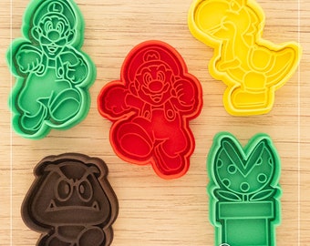 Puede incluir: Cinco cortadores de galletas diferentes, cada uno con un personaje diferente de la franquicia de videojuegos Super Mario Bros. Los cortadores son verdes, rojos, amarillos, marrones y verdes. Los personajes son Mario, Luigi, Yoshi, un Goomba y una planta Piraña.