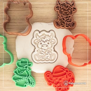 May include: A set of five cookie cutters, including a highland cow, a cowboy, a Christmas tree, a flower, and a heart. The cookie cutters are made of red, green, brown, and white plastic.