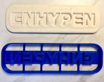 May include: A blue plastic cookie cutter with the word "ENHYPEN" embossed in white. The cutter is designed to create cookies with the same lettering.