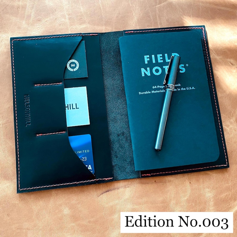 May include: Black leather wallet with red stitching, featuring multiple card slots and a pocket for a notebook. The wallet is open to reveal a black Field Notes notebook with a black pen and the text "FIELD NOTES" in white.