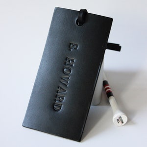 Puede incluir: Etiqueta de cuero negro con el texto "S. HOWARD" en relieve en blanco.