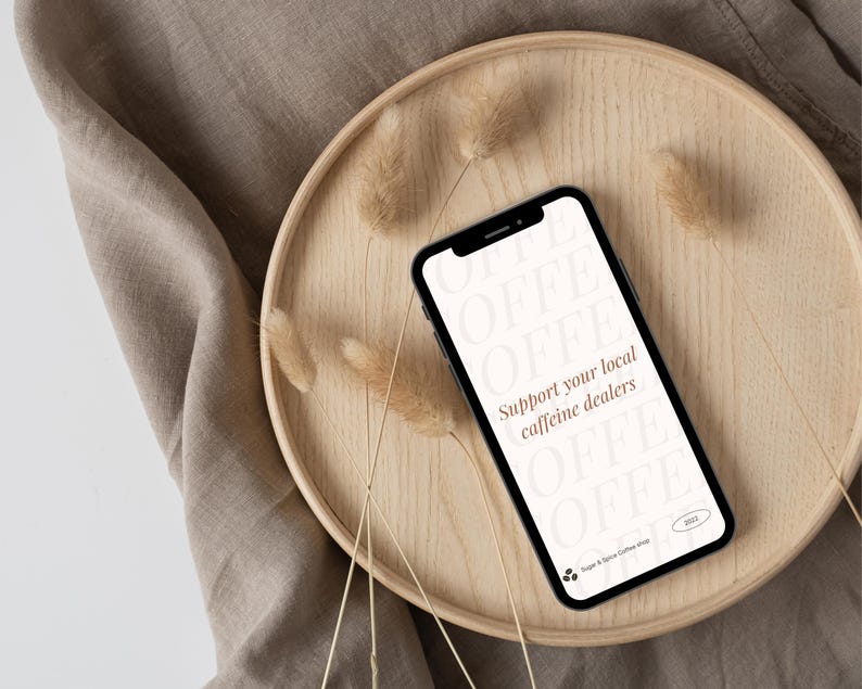 以下が含まれることがあります： 黒い画面に「Support your local caffeine dealers」というテキストが表示された白いスマートフォン。周囲には茶色のフォントで「COFFEE」という単語が並んでいます。スマートフォンは、乾燥した草が敷かれた木製のトレイの上に置かれています。