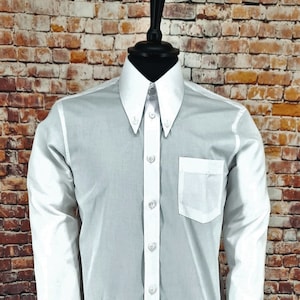 Puede incluir: Una camisa blanca de manga larga con botones, cuello blanco y bolsillo blanco en el lado izquierdo. La camisa tiene cuello abotonado y puños abotonados.