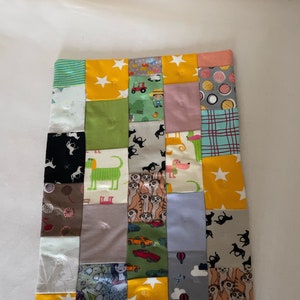 Könnte beinhalten: Eine Patchwork-Decke mit einer Vielzahl von bunten Stoffen mit Tier-, Auto- und anderen Motiven. Die Decke besteht aus Quadraten und Rechtecken, und die Nähte sind sichtbar. Die Decke ist gelb, grün, blau, rosa, braun und weiß.